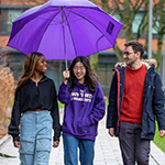 Three students with under a purple umbrella